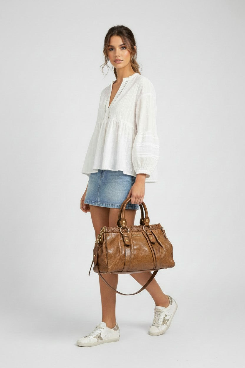 Model in a white blouse carrying a brown leather Miu Miu tote bag